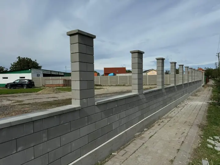 Szürke díszzsalukő kerítés lábazat és magas pillérek fedkővel hosszú utcafronton
