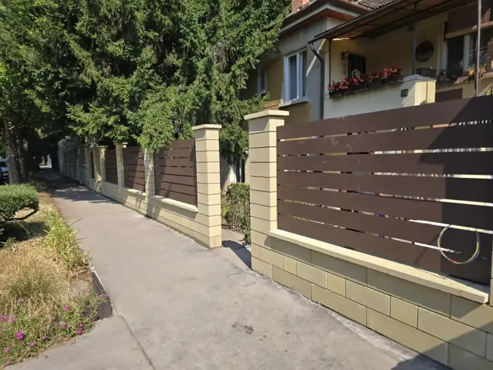 Homokszínű díszzsalukő kerítés barna vízszintes lécmezőkkel kertes utcafronton